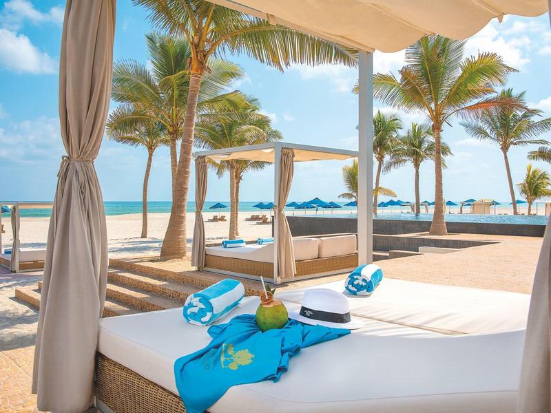 Luxury beach bed with blue towels and view of palm trees and sea on a sunny day.