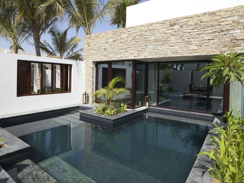 Modern pool area with smooth stone walls and tropical plants at a white house.