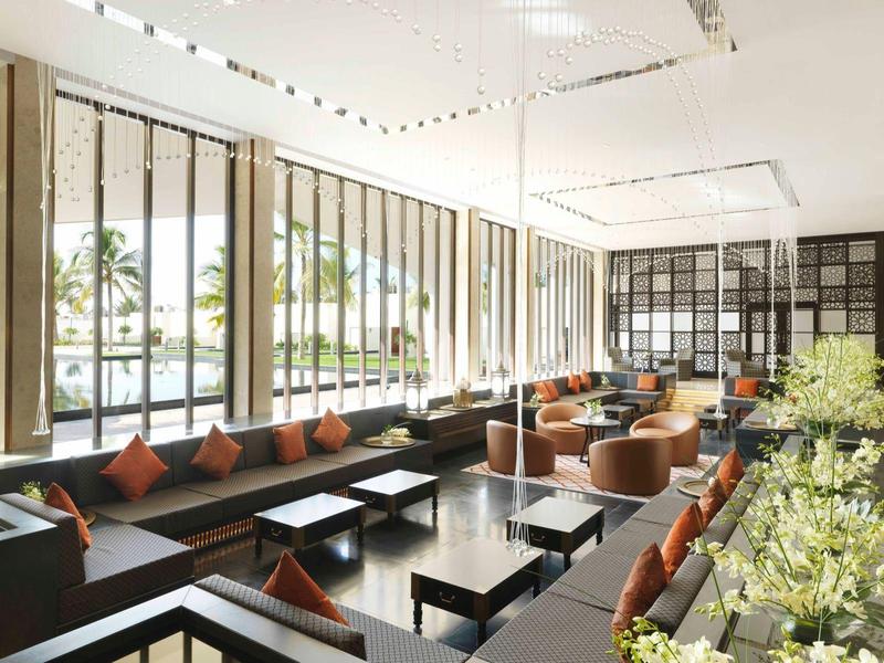 Modern hotel lounge with large windows, long sofas, and round armchairs beside tables.
