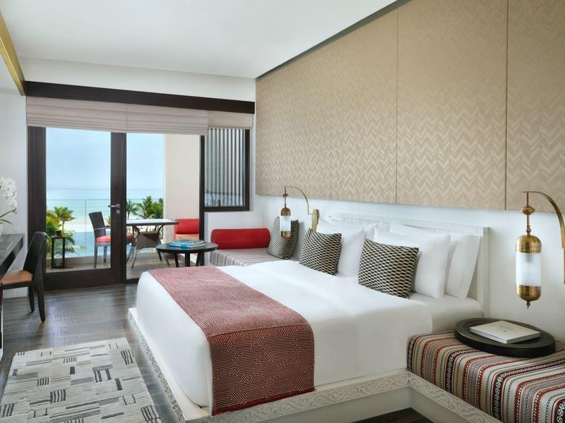 Modern hotel room with large bed, balcony, and ocean view.
