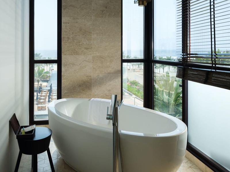 Modern bathtub by large windows with city and sea view in a luxurious bathroom.
