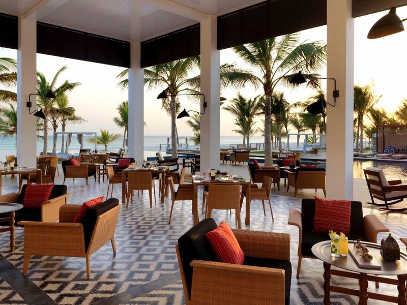 Modern restaurant with large windows overlooking pool and palm trees.