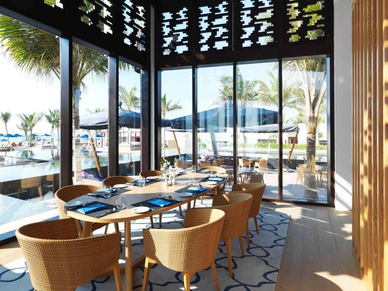 Modern restaurant with large windows overlooking pool and palm trees.