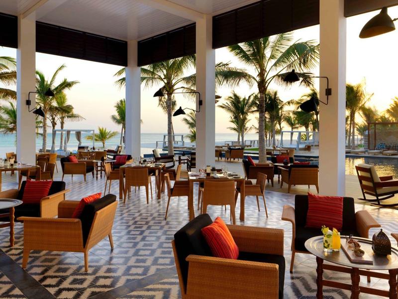 Open restaurant area with chairs and tables, palm trees, and sunset in the background.