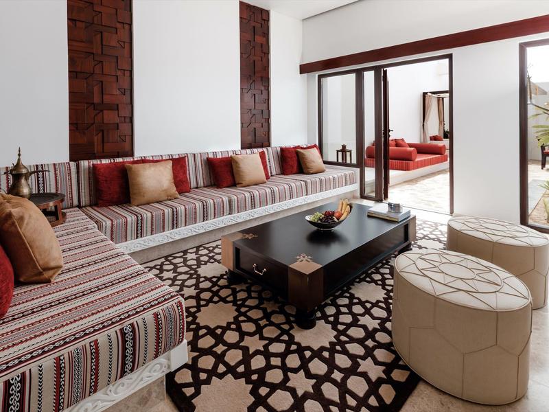Bright living room with patterned sofas, coffee table, and terrace access overlooking greenery.
