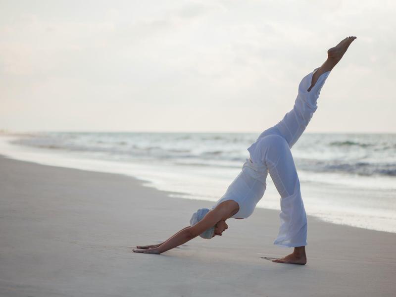 Person performing yoga pose on beach with ocean in the background.