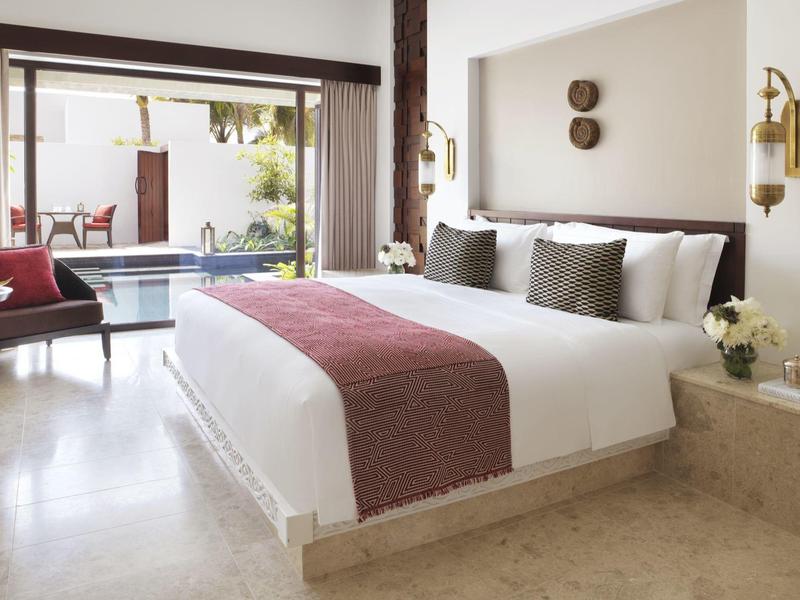 Bright hotel room with large bed, seating area, and pool view.