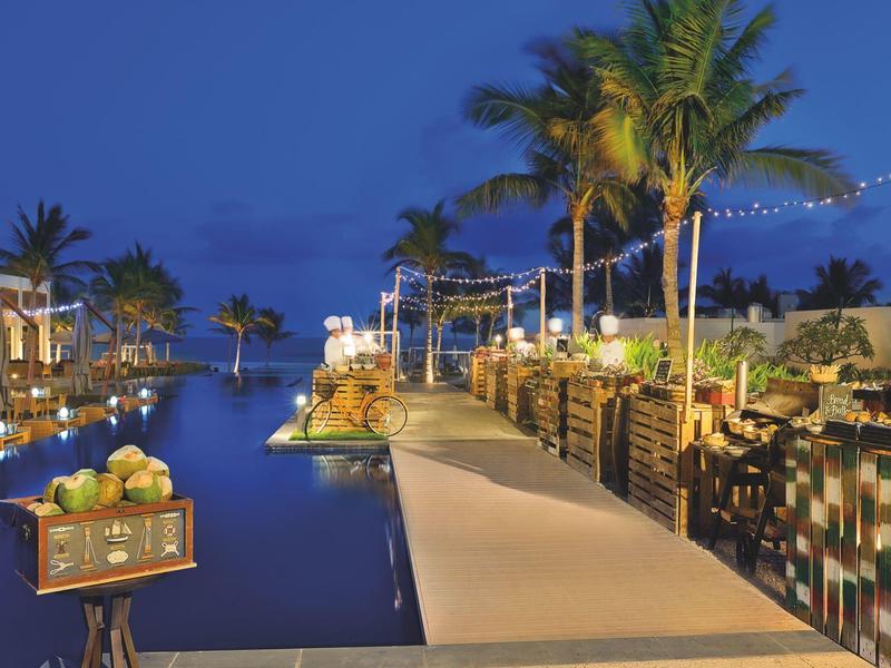 Evening pool area with palm trees, lights, and seating by the water.