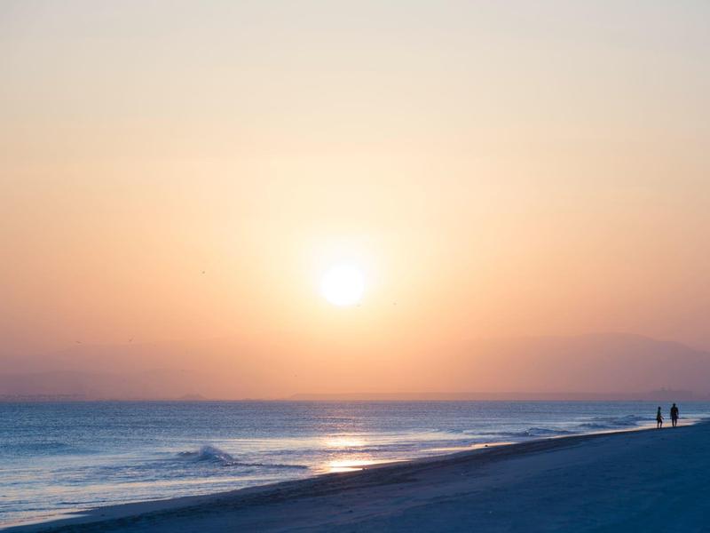 Sunset over calm beach with two people near the water.