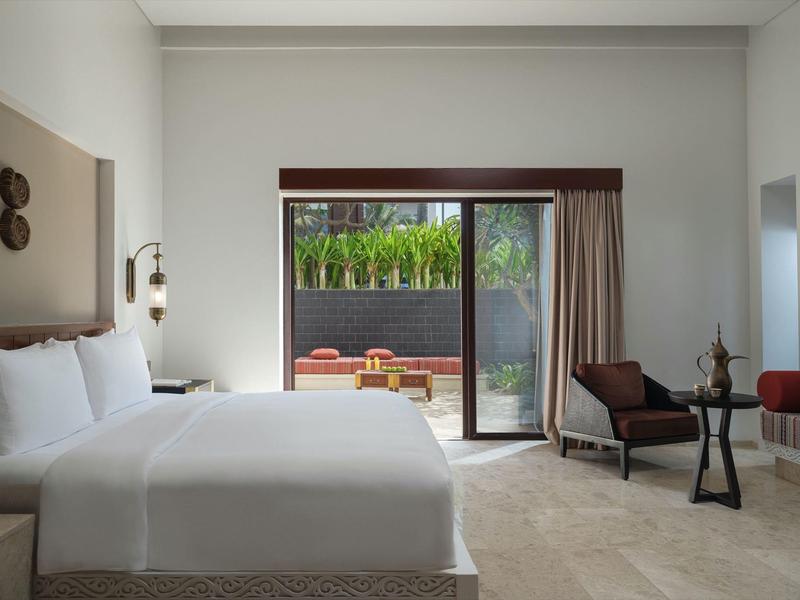 Modern hotel room with a large bed, armchairs, and terrace access with garden view.