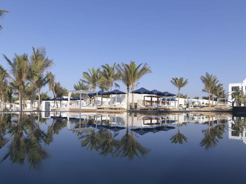 Luxury pool with palm trees and sun loungers under clear sky reflected in water.