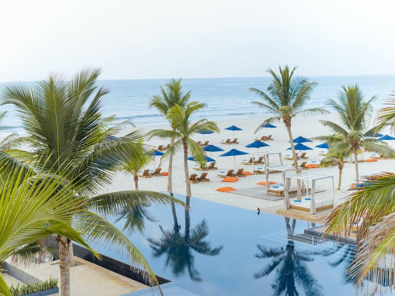 Infinity pool and beach with palm trees and umbrellas by the sea.