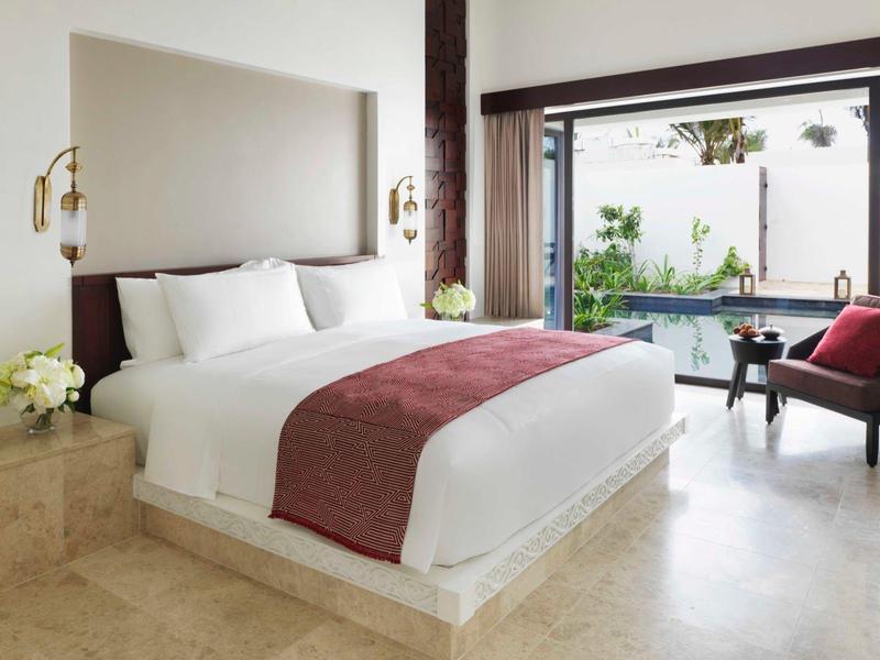 Modern hotel room with large bed, lounge chair, and view of pool and garden.