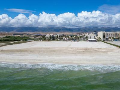 Weitläufiger Sandstrand mit leichtem Wellengang, dahinter Stadt und Berge unter blauem Himmel.