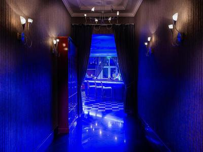 Donkere hotelgang met blauw verlichte vloer en uitzicht op een verlichte nachtclub.