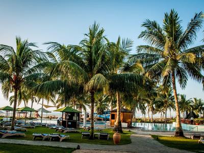 Palmen stehen an einem Pool mit Liegestühlen und Sonnenschirmen unter klarem Himmel.