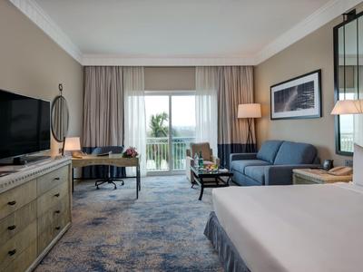 Modernes Hotelzimmer mit Doppelbett, Sofa, Schreibtisch, TV und Balkon mit Meerblick.