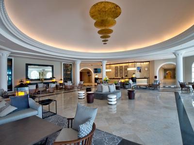 Ruime, elegante hotel lobby met banken, fauteuils en moderne plafondverlichting.