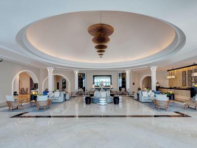 Großzügige Hotellobby mit runder Decke, modernem Kronleuchter, Sofas und großen Fenstern.