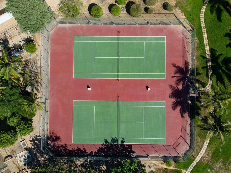 Luftaufnahme von zwei nebeneinanderliegenden Tennisplätzen mit grünem Spielfeld und rotem Rand.