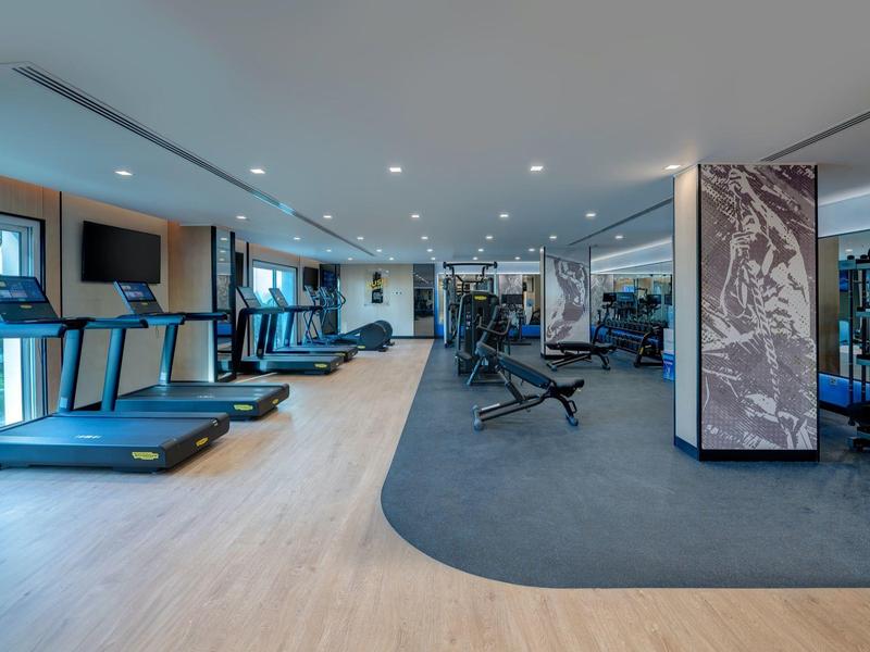 Moderner Fitnessraum mit Laufbändern, Kraftgeräten und Spiegeln in einem Hotel.