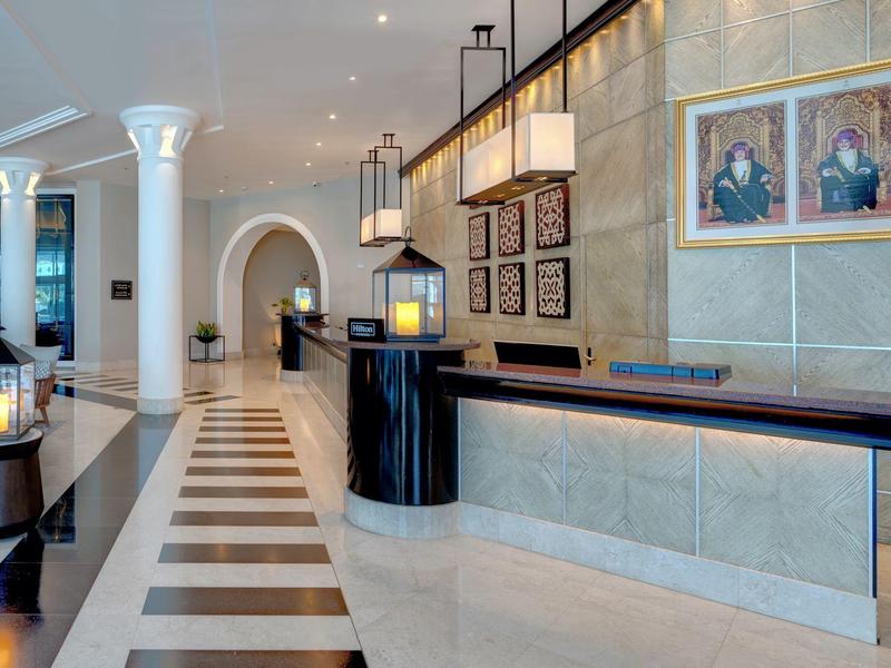 Elegante Hotellobby mit langer Rezeption, Säulen und moderner Beleuchtung in hellem Ambiente.