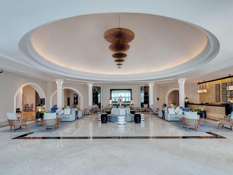 Großzügige Hotellobby mit runder Decke, modernem Kronleuchter, Sofas und großen Fenstern.