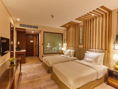 Modernes Hotelzimmer mit zwei Einzelbetten, Holzelementen und warmem Licht.