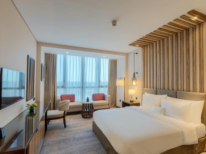 Modernes Hotelzimmer mit großem Bett, Holzakzenten und zwei Sesseln am Fenster.