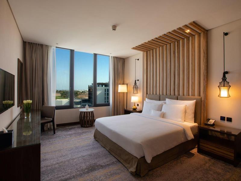 Modernes Hotelzimmer mit großem Bett, Holzverkleidung, Fensterblick und stilvoller Beleuchtung.