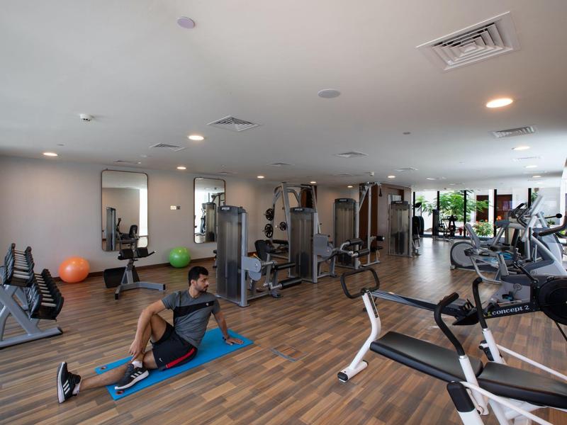 Großer Fitnessraum mit Holzfußboden, Geräten, Spiegeln und zwei Personen, die Sportübungen machen.