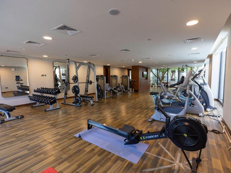 Großer Fitnessraum mit Holzboden, Spiegelwänden, Rudergerät, Laufbändern und Kraftgeräten.