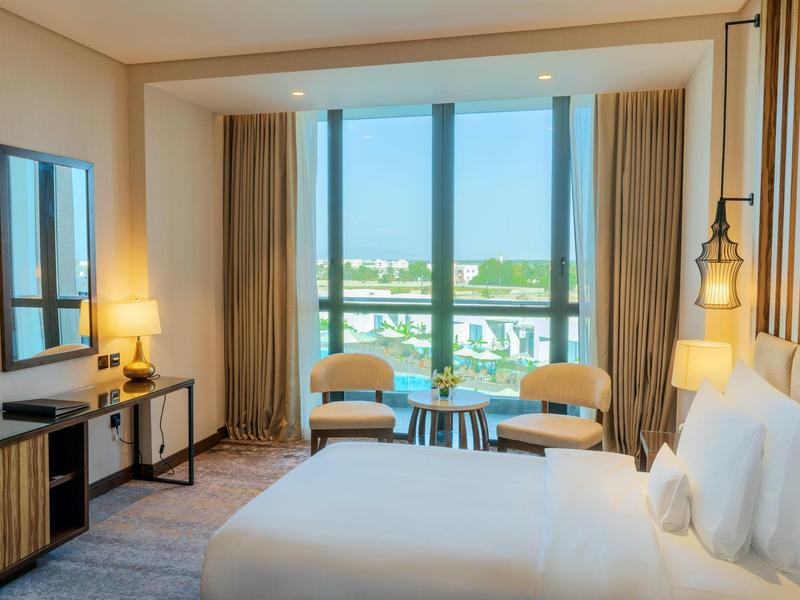 Helles Hotelzimmer mit großem Fenster, Doppelbett, zwei Stühlen und modernem Mobiliar.