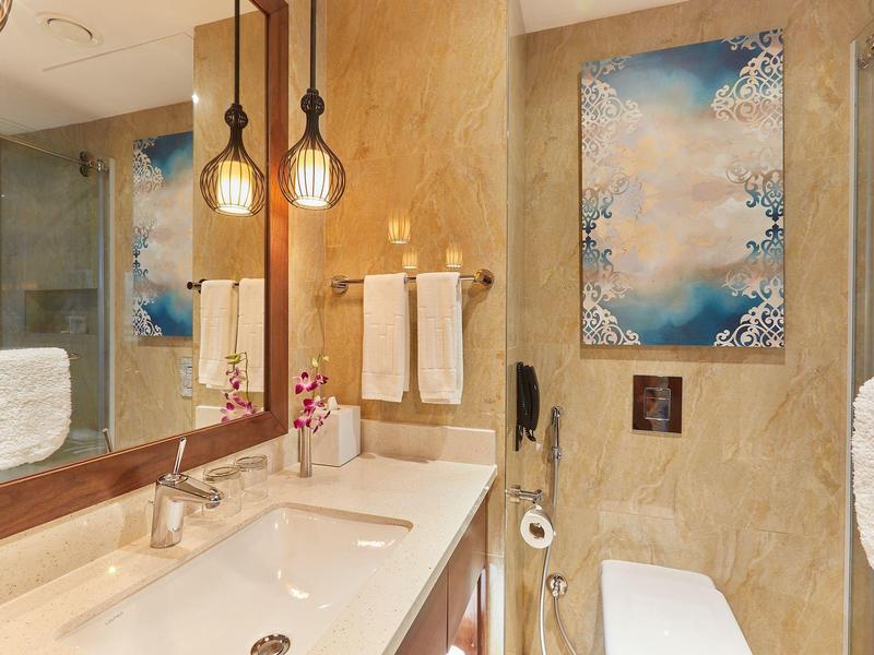 Moderner Badezimmerspiegel mit Doppelwaschbecken, goldene Wandleuchten und blauer Kunstdruck an Wand.