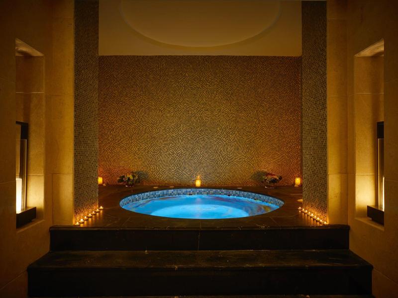 Helles, rundes Whirlpool-Becken mit blauer Beleuchtung in dunklem, luxuriösem Raum mit warmem Licht.