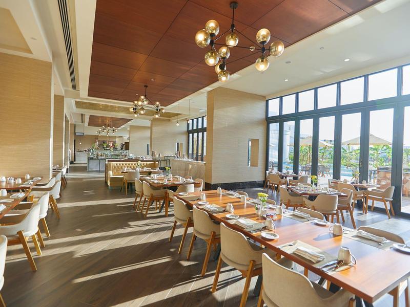 Helles Restaurant mit großen Fenstern, Holzdecken, modernen Lampen und Tischreihen mit Stühlen.