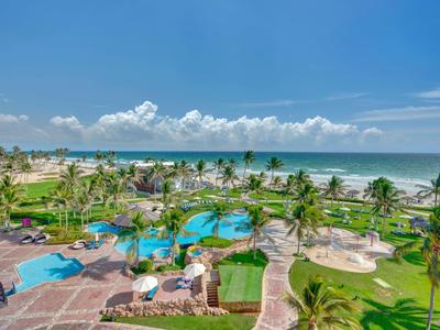 Vista di area piscina tropicale con palme e spiaggia sul mare sotto il cielo azzurro