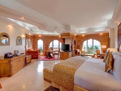 Ampia camera d'hotel con grande letto, zona salotto e grandi finestre che si affacciano sul paesaggio.