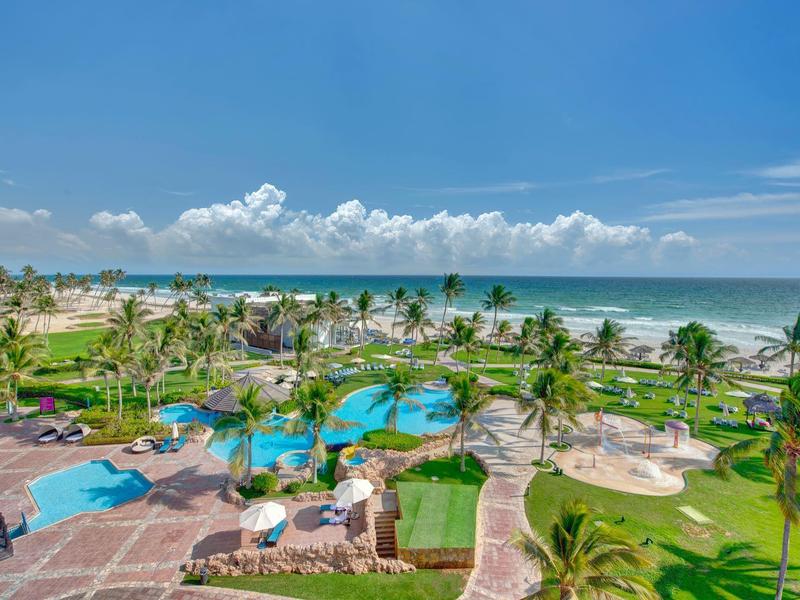 Vista di area piscina tropicale con palme e spiaggia sul mare sotto il cielo azzurro