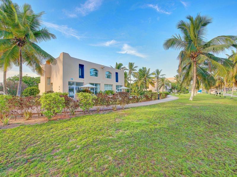Edificio dell'hotel circondato da palme e prato verde sotto cielo sereno.