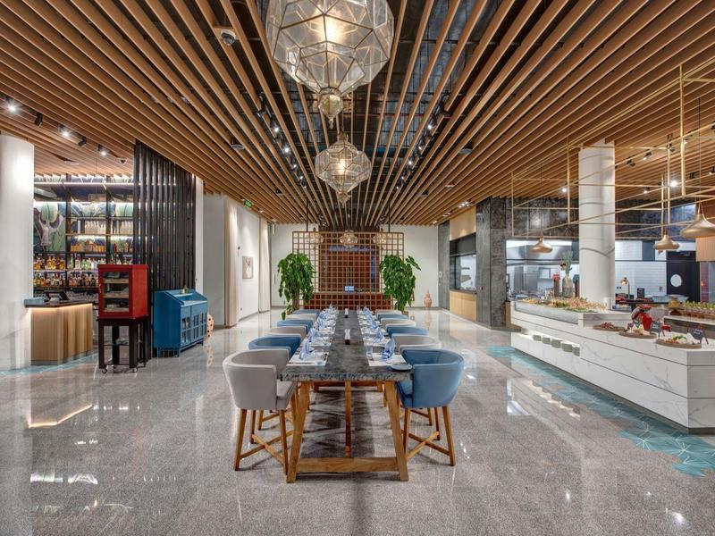 Area pranzo moderna con tavolo lungo in legno e sedie blu sotto lampade sul soffitto in legno.