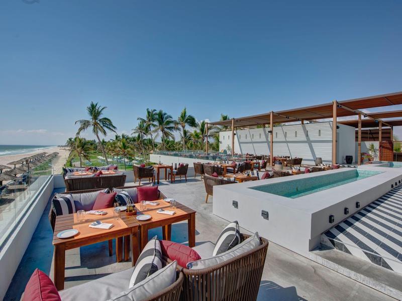 Ristorante all'aperto con posti a sedere e vista sulla spiaggia sotto un cielo sereno.