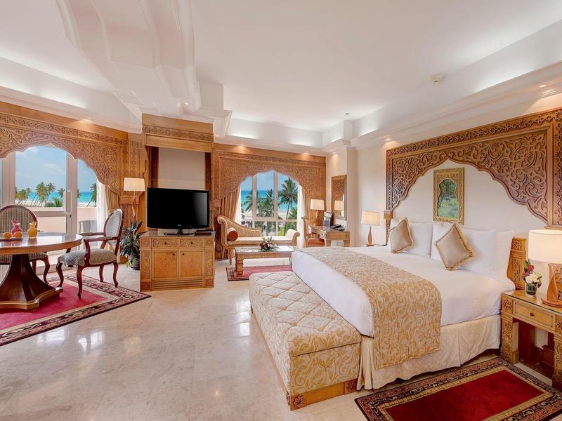 Elegante camera d'hotel con letto grande, zona salotto e elementi decorativi in toni caldi.