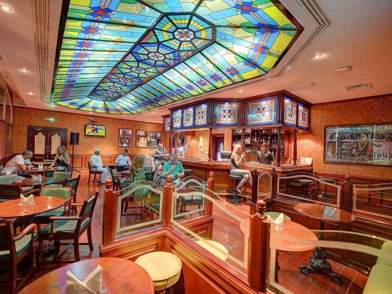 Accogliente bar con soffitto in vetro colorato e mobili in legno sotto luce calda.