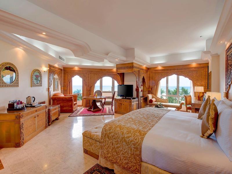 Ampia camera d'hotel con grande letto, zona salotto e grandi finestre che si affacciano sul paesaggio.