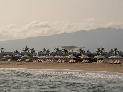 Plage avec chaises longues et parasols devant des montagnes au bord d'une mer calme.