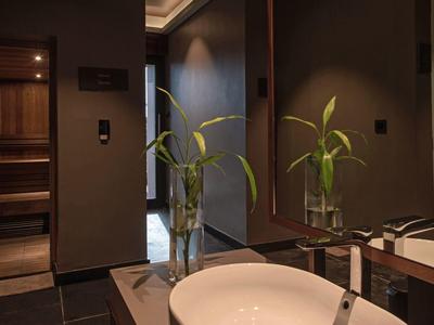 Salle de bain moderne avec lavabo rond devant un grand miroir et accès à un sauna.