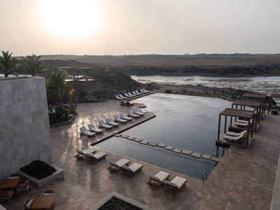 Piscine extérieure moderne avec chaises longues et vue sur un paysage fluvial paisible au coucher du soleil.
