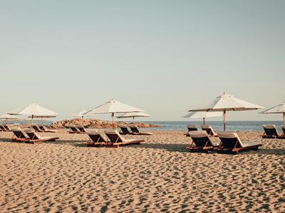 Alignement de chaises longues avec parasols blancs sur une plage de sable au bord de la mer.