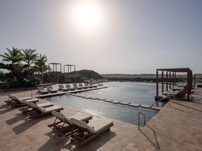 Zona de piscina con tumbonas y sombras al atardecer en un complejo hotelero.